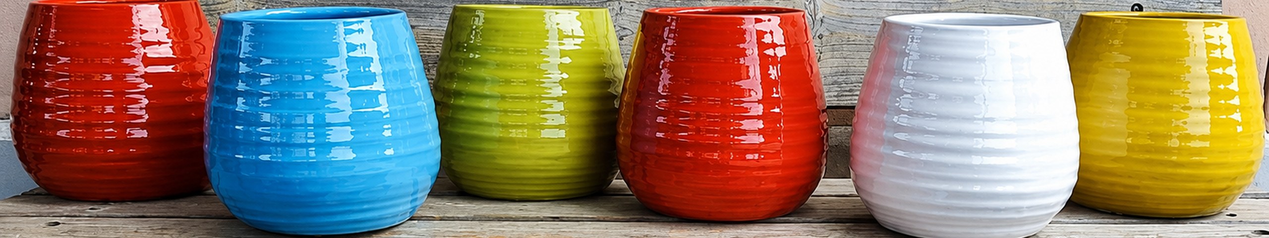 Vasi in ceramica smaltata nei colori rosso, azzurro, verde, bianco e giallo allineati su una panca in legno