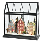 La lanterna accesa vista di tre quarti: case colorate con finestre illuminate a LED, abeti innevati e figure in miniatura