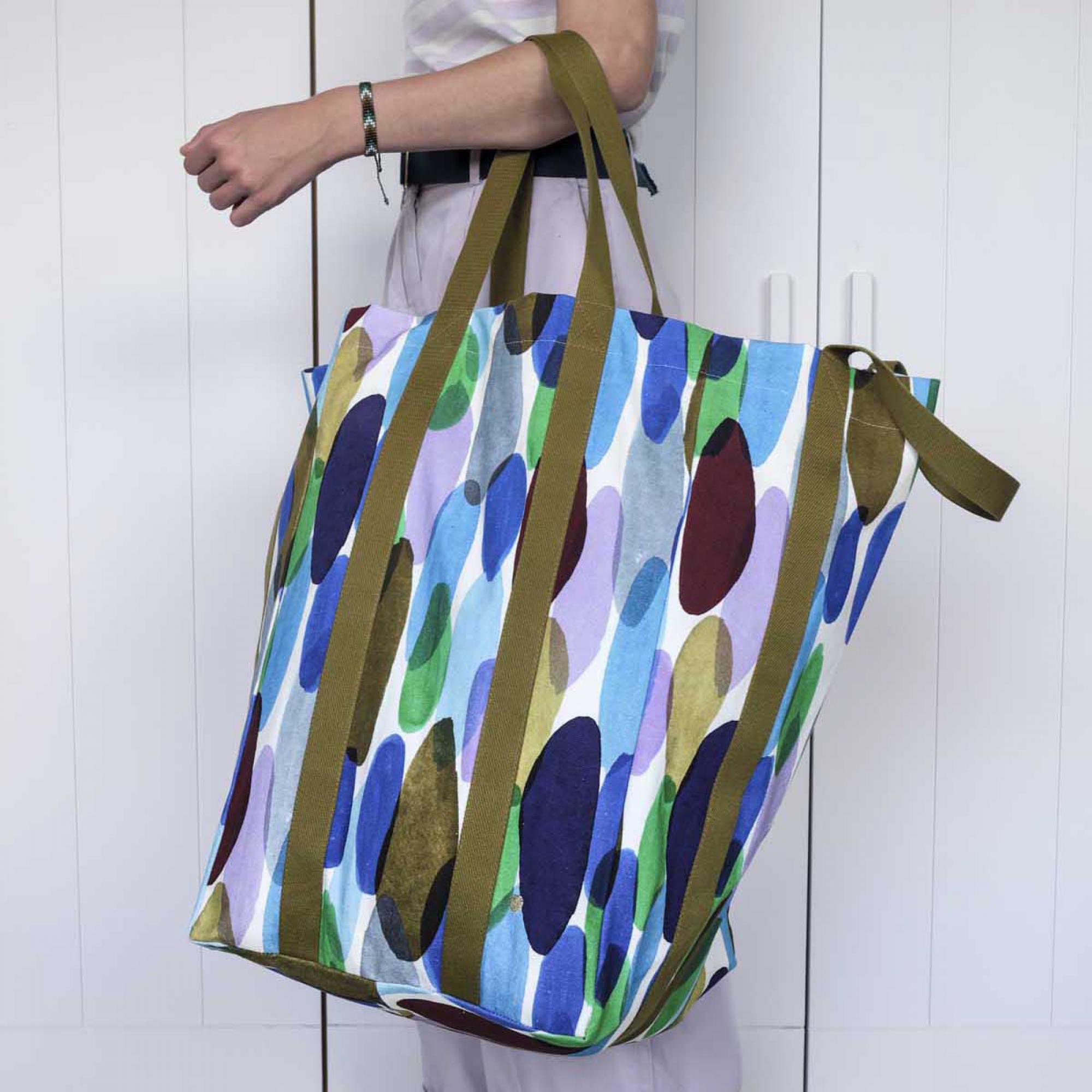 Borsa Maxi Poppins con stampa Joy Joy multicolore portata a spalla davanti a una porta chiara: si vedono la lunghezza dei manici e il volume della borsa in uso.