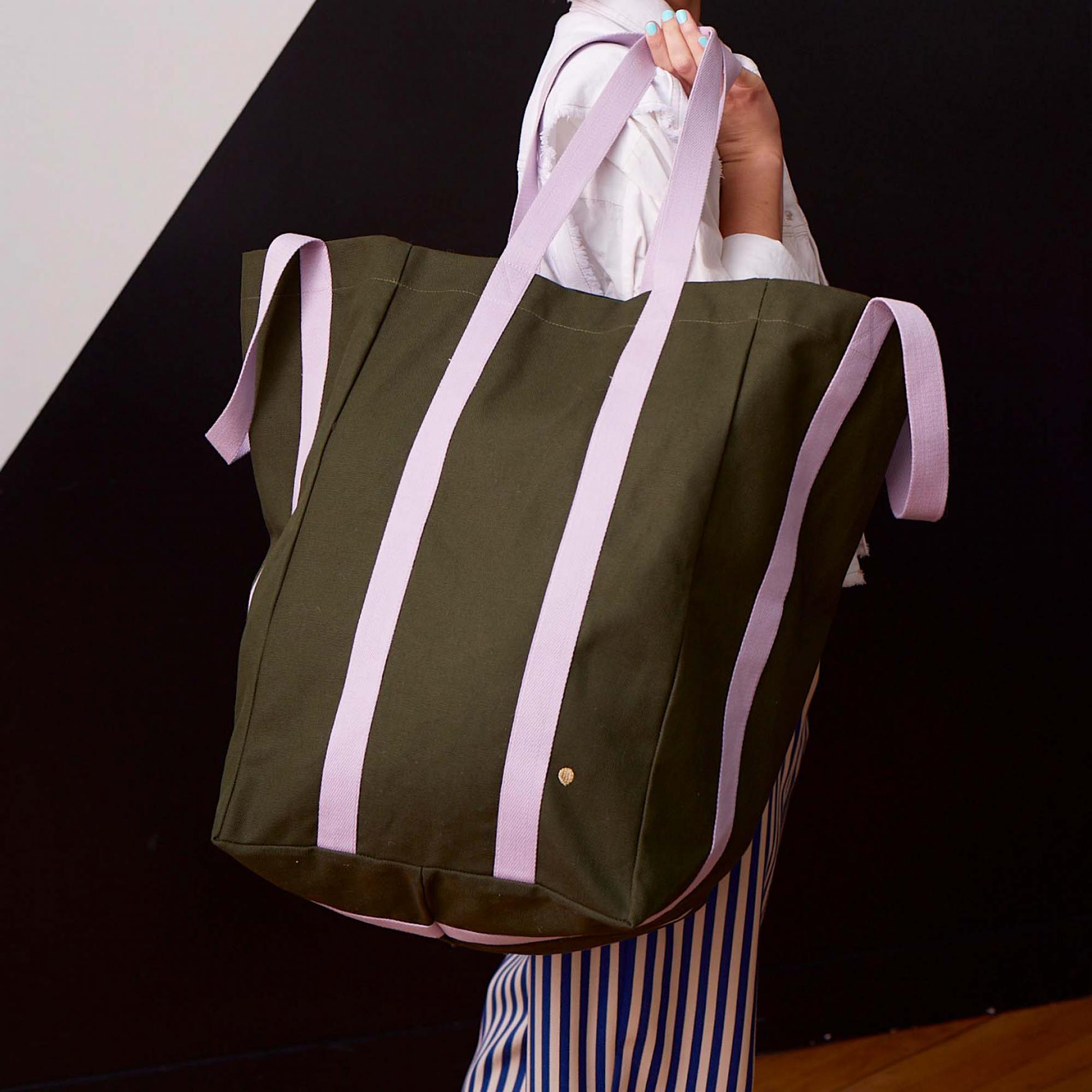 Borsa Maxi Poppins verde oliva con manici lilla portata a spalla da una persona: la foto mostra la capienza reale e la caduta della tela quando la borsa è piena.