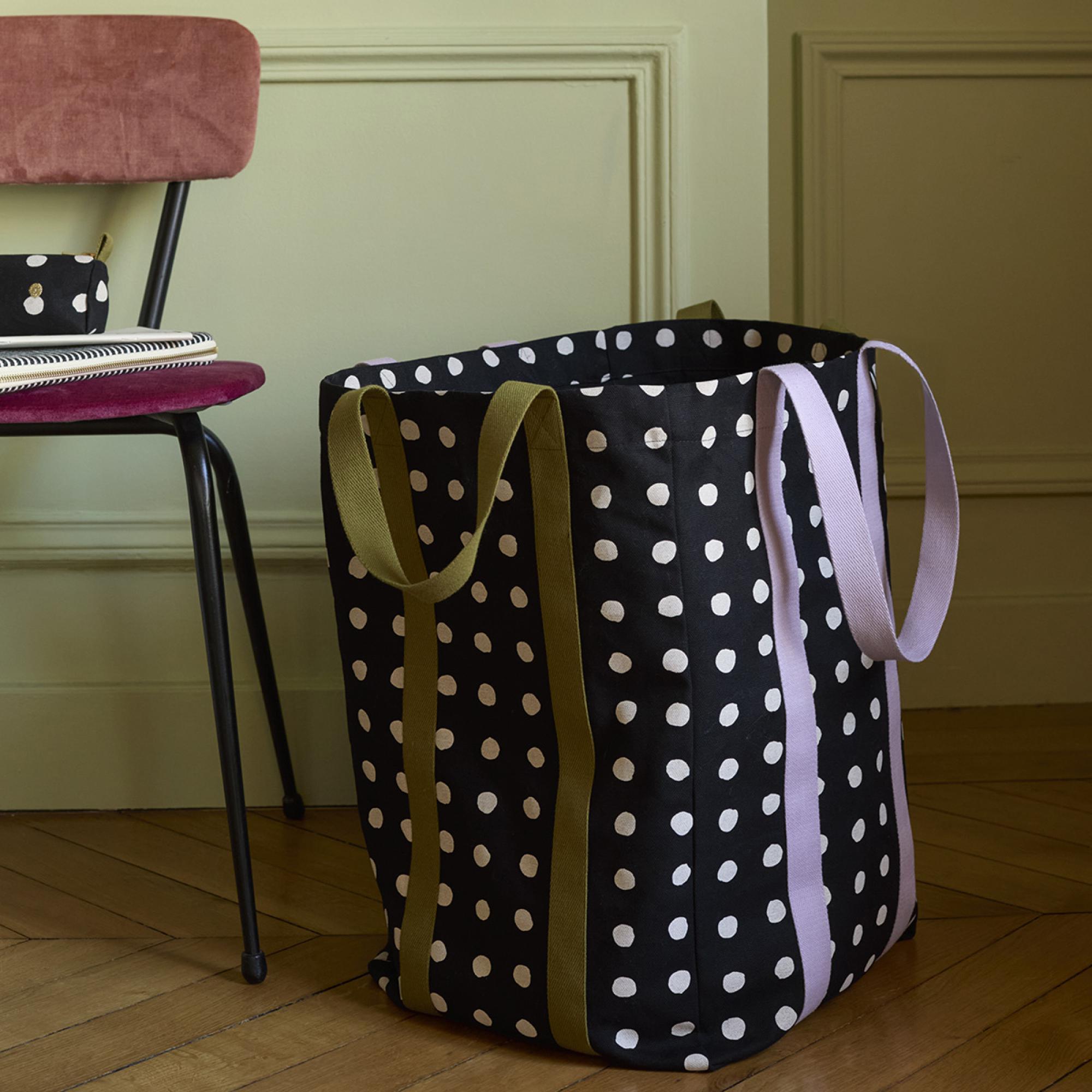 Borsa Maxi Poppins nera a pois bianchi appoggiata a terra accanto a una sedia, davanti a una parete verde salvia: la borsa è il prodotto in vendita, sedia e arredi non sono compresi.