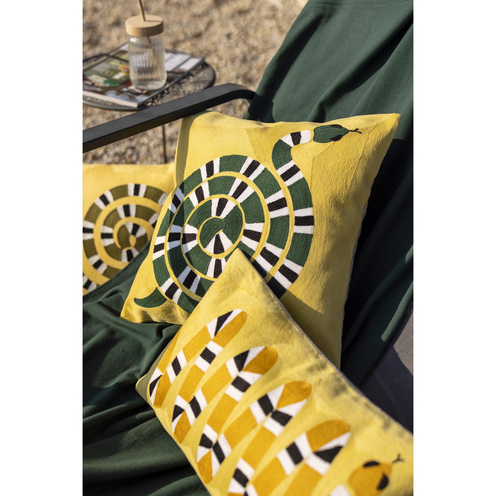 Dettaglio del ricamo in rilievo dei cuscini Yoka giallo mango su una sdraio da giardino con plaid verde scuro: si riconoscono la doppia spirale del 40 × 65 cm, la spirale verde del 45 × 45 cm e il serpente ocra a zigzag del 30 × 50 cm. Fotografia di catalogo del marchio Vivaraise.