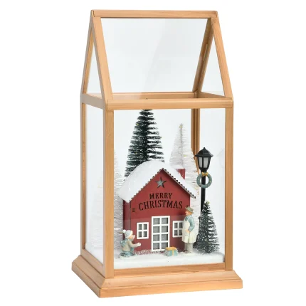 Lanterna natalizia verticale a serra con struttura in plastica color legno chiaro, a luci spente, su fondo bianco: una casetta rossa con la scritta Merry Christmas sul fronte, abeti innevati e un lampione.