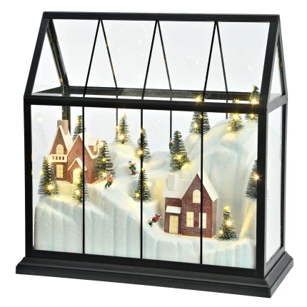 Lanterna natalizia in plastica nera a forma di serra, accesa: i LED bianchi caldi illuminano gli abeti, le finestre delle due case in mattoni e il pendio innevato percorso dagli sciatori. Misura 33 cm di larghezza e 33 cm di altezza.