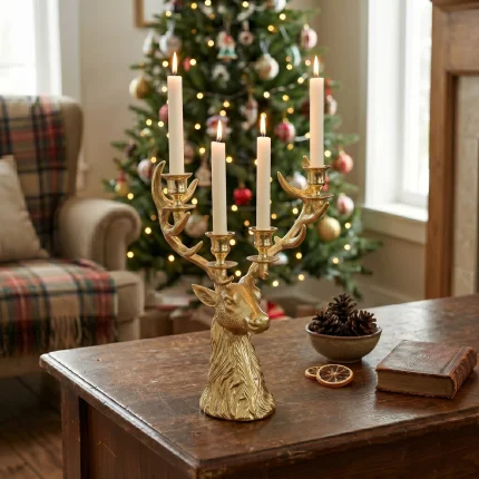 Il portacandele testa di cervo dorato con quattro candele accese su un tavolo di legno scuro, davanti a un albero di Natale illuminato e a una poltrona con plaid scozzese; accanto una ciotola di pigne, fette di arancia essiccata e due libri. Candele, tavolo, albero, poltrona, plaid, ciotola, pigne, arance e libri non sono compresi.