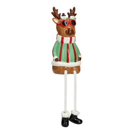 Figura decorativa di renna in ceramica su fondo bianco: testa con corna e occhiali da sole scuri, corpo con maglione a righe verdi, bianche e rosse, e due gambe pendenti in metallo che terminano con scarpe nere.