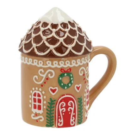 Tazza in ceramica color biscotto a forma di casetta di pan di zenzero, su fondo bianco: finestre e bastoncini di zucchero dipinti in bianco e rosso, manico beige, coperchio modellato come un tetto di tegole innevate.