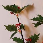 Dettaglio di foglie di agrifoglio, bacche rosse e LED bianco caldo del ramo luminoso