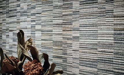 Parete rivestita con la carta da parati Ikulu Stone (W929/02): una parete ripresa da vicino con rami e fiori secchi in primo piano. Gli altri oggetti della scena non sono compresi nella vendita.