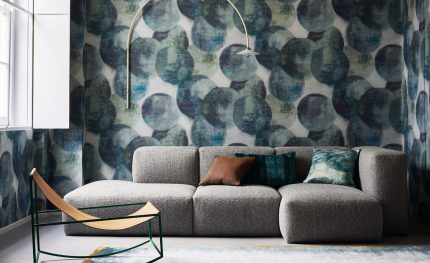 Parete rivestita con la carta da parati Lune Peacock (W931/02): un soggiorno con divano grigio, poltrona e lampada ad arco. Gli altri oggetti della scena non sono compresi nella vendita.