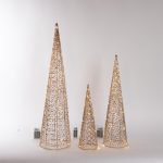 Set di tre coni luminosi di Natale in metallo dorato alti 40, 60 e 80 cm, accesi con LED bianco caldo, con i portabatterie visibili, su fondo chiaro