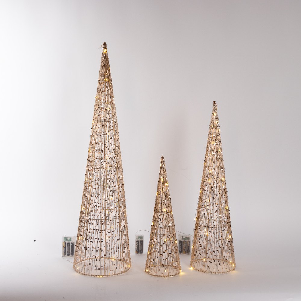 Set 3 coni luminosi di Natale oro 40, 60 e 80 cm Set di tre coni luminosi di Natale in metallo dorato alti 40, 60 e 80 cm, accesi con LED bianco caldo, con i portabatterie visibili, su fondo chiaro