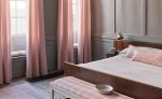 Camera da letto con tende e cuscini nei tessuti in cotone della collezione Kemble di Romo, nei toni del rosa. In vendita c’è soltanto il tessuto al metro: arredi e complementi della scena non sono compresi.