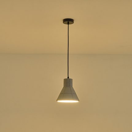 Lampada a sospensione Arme in cemento grigio sfaccettato, diametro 20 cm, accesa contro una parete chiara. La lampadina non è compresa