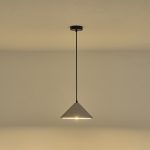 Lampada a sospensione Platre in cemento grigio plissettato, diametro 25 cm, accesa contro una parete chiara. La lampadina non è compresa