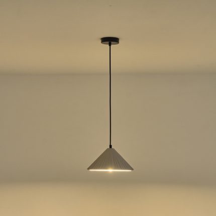 Lampada a sospensione Platre in cemento grigio plissettato, diametro 25 cm, accesa contro una parete chiara. La lampadina non è compresa