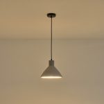 Lampada a sospensione Yeso in cemento grigio a cono, diametro 24 cm, accesa contro una parete chiara. La lampadina non è compresa