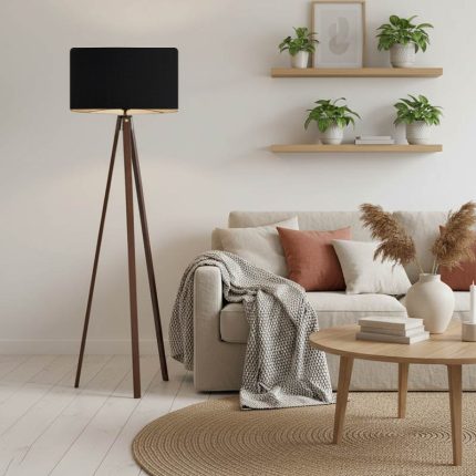 Lampada da terra a treppiede in legno noce con paralume nero accanto a un divano in soggiorno; divano, tavolino, tappeto, piante e oggetti della scena non sono compresi
