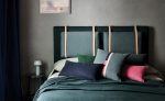 Camera da letto con testiera imbottita in tessuto Linara di Romo grigio ardesia, tende scure e cuscini Linara in blu, verde e rosa. In vendita c’è soltanto il tessuto al metro: arredi e complementi della scena non sono compresi.