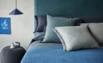 Camera da letto con testiera, copriletto e cuscini in tessuto Linara di Romo nei toni del blu e del grigio azzurro. In vendita c’è soltanto il tessuto al metro: arredi e complementi della scena non sono compresi.