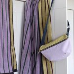 Maxi telo bagno Charly Lilas appeso a un gancio accanto a una borsa; gli altri oggetti della scena non sono compresi