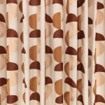 Il velo Omri di Villa Nova nella colorazione Umber drappeggiato in pieghe morbide: semicerchi ricamati terra d’ombra, rosa cipria e cammello su fondo écru.