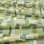 Il tessuto stampato in cotone e lino Nira di Villa Nova nella colorazione Canopy drappeggiato in pieghe morbide: blocchi ad acquerello nei verdi salvia, oliva e muschio, con tocchi di giallo, su fondo écru.