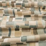 Il tessuto stampato in cotone e lino Nira di Villa Nova nella colorazione Mineral drappeggiato in pieghe morbide: blocchi ad acquerello sabbia, tortora, grigio e salvia su fondo écru.