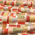 Il tessuto stampato in cotone e lino Nira di Villa Nova nella colorazione Plume drappeggiato in pieghe morbide: blocchi ad acquerello rosso, corallo, rosa, ocra e salvia su fondo écru.