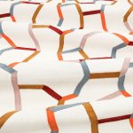 Il tessuto ricamato Samir di Villa Nova nella colorazione Plume drappeggiato in pieghe morbide: linee ricamate arancio, ruggine, grigio azzurro e cipria su fondo écru.