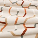 Il tessuto ricamato Samir di Villa Nova nella colorazione Sienna drappeggiato in pieghe morbide: linee ricamate ocra, ruggine, cammello e grigio su fondo crema.